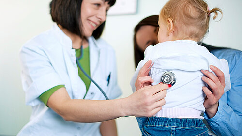 A mother holding a child whilst a GP examines them