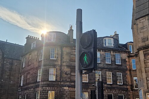 A Green Man signal at Pilrig Street with the sun and tenements in the background