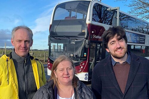 Three people standing in front of a bus