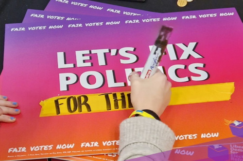 A poster reading "Let's Fix Politics", with someone in the process of writing "For Our NHS" underneath it