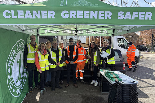 Group of people standing under a gazebo with cleaner, greener, safer on it