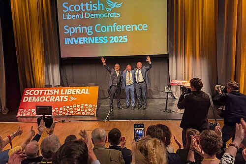 Alex Cole-Hamilton, Jamie Greene and Ed Davey cheering in front of a crowd of clapping Lib Dem party members.