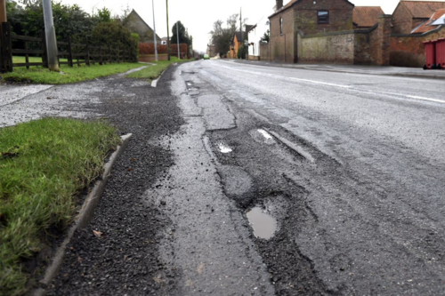 Pothole-damaged road surface with multiple cracks and broken tarmac along the edge of the carriageway in North Lincolnshire.