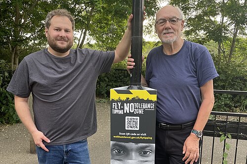 Liberal Democrat campaigners Alex Lewis and Alan Jones standing by a new fly-tipping sign