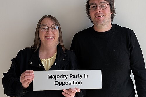 Heather Fagan and Paul Edgeworth holding a sign saying 'Majority Party in Opposition'