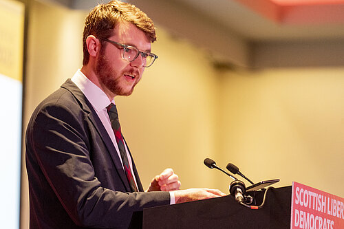 Daniel Khan-O'Malley at a podium speaking.