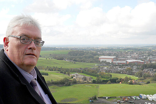 Howard Sykes in front of view of the countryside above Shaw, with the town in the background 
