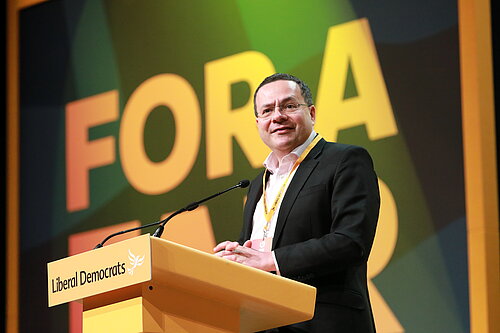 Mark Pack. Mark is photographed stood at the podium at Liberal Democrat conference.