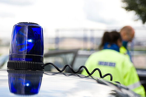 Police officers in the background, with a blue light on a vehicle in the foreground 