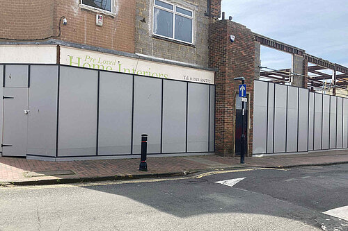 Boarded up facades with one building hollowed out behind, of what used to be a thriving shopping parade