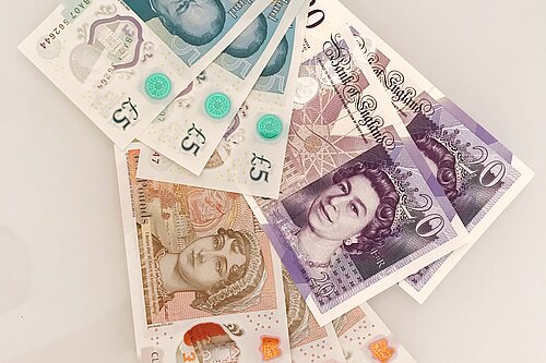 Seven pound coins on top of a ten pound note.