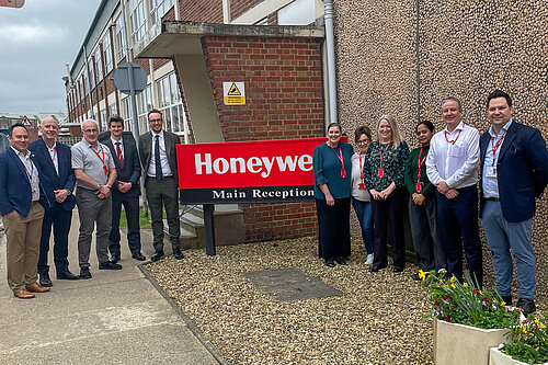 A group of employees and visitors stand outside the Honeywell main reception building beside a large company sign