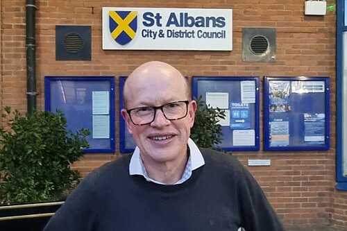 Councillor Paul de Kort is standing in front of the St Albans District Council building, smiling and looking directly at the camera.