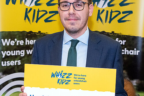 Tom Gordon MP holding a sign supporting Whizz Kids Charity