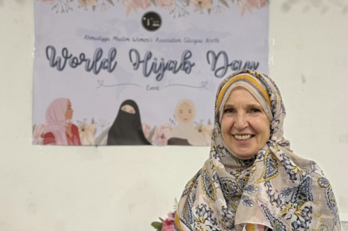 Susan Murray wearing a light coloured Hijab with a poster in the background for World Hijab Day